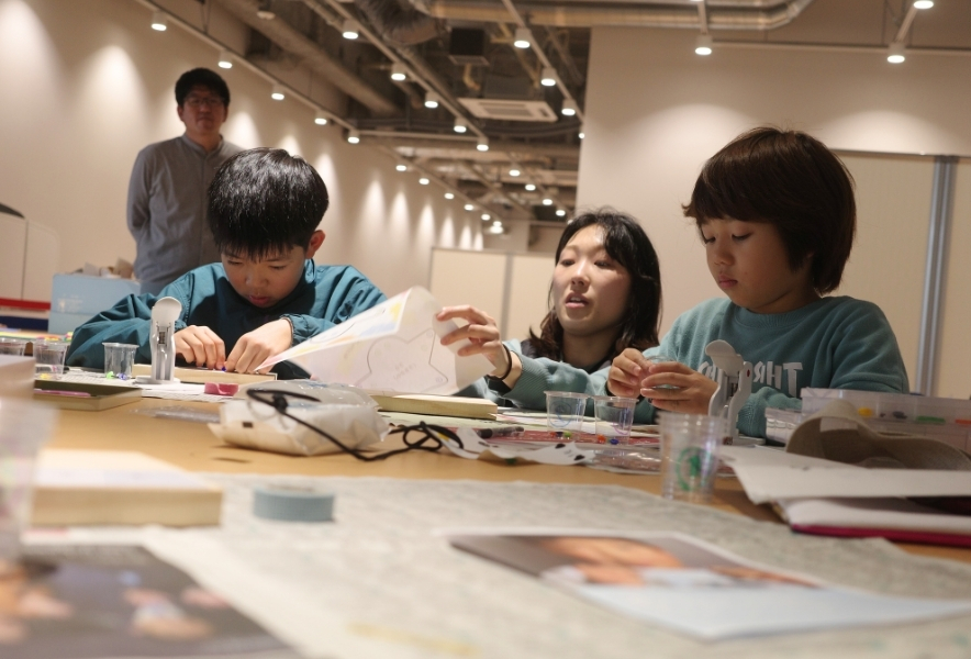 子どもたちが真剣な表情で、廃材からミニポーチをつくるワークショップの様子。