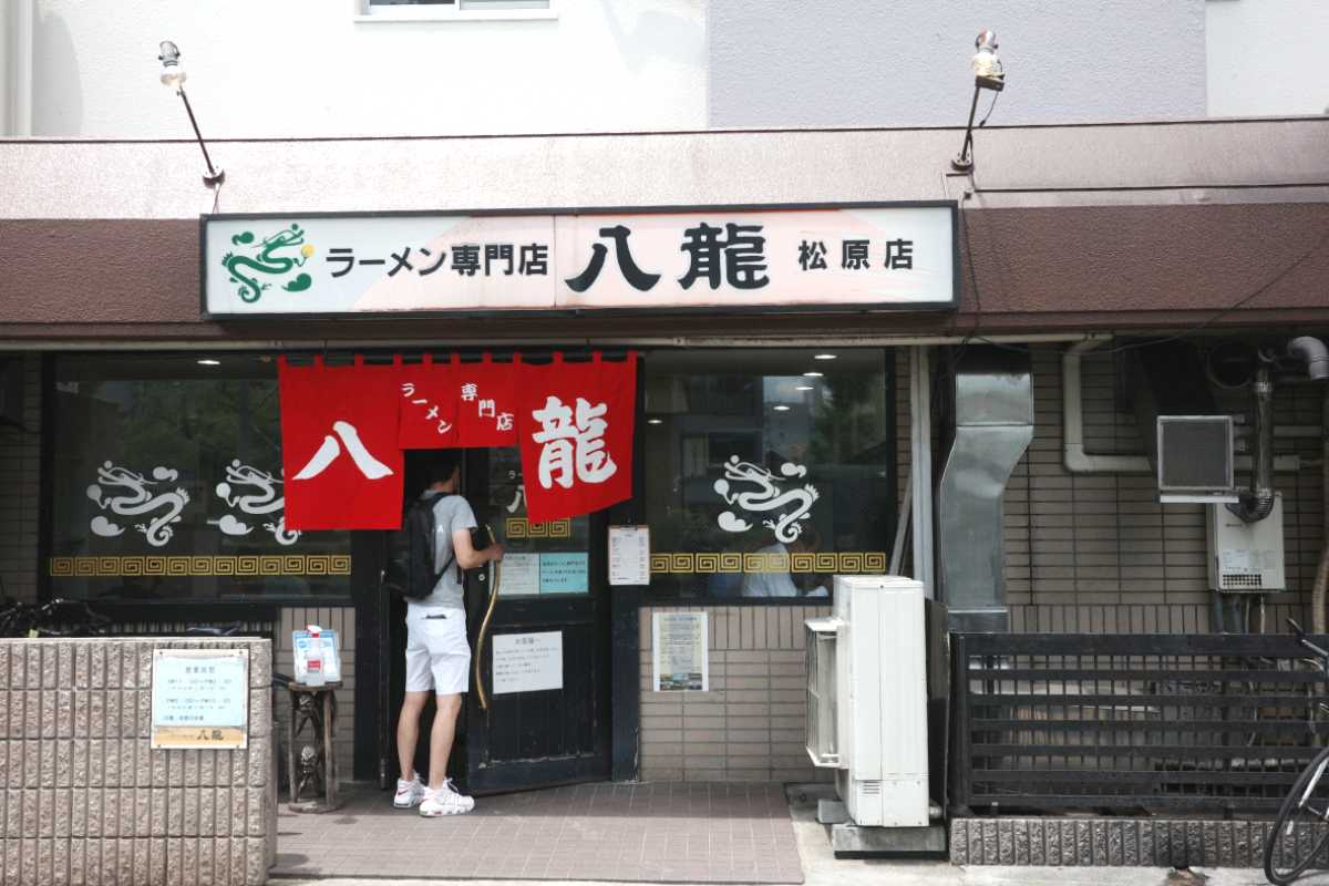 名古屋・松原にあるラーメン専門店「八龍」の入り口。赤いのれんをくぐって入店する常連の姿。