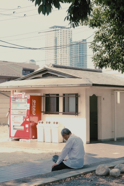 覚王山日泰寺の境内。赤い自動販売機の前で木陰に座り休む男性。背景には高層マンションが見える。