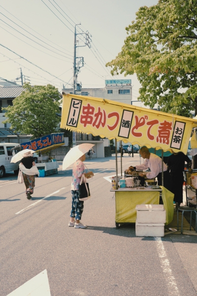 覚王山日泰寺の縁日。黄色いテントの屋台で串カツやどて煮を買う人の姿。