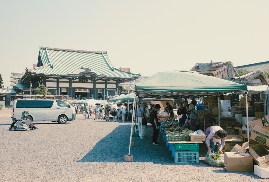 覚王山日泰寺の境内で開かれる弘法さんの縁日。青いテントの下には野菜や日用品を売る露店が並び、多くの人でにぎわう光景。