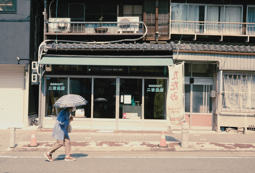 覚王山日泰寺周辺の商店街。ふすま店の古い店構えの前を日傘を差した人が歩く、下町の風景。