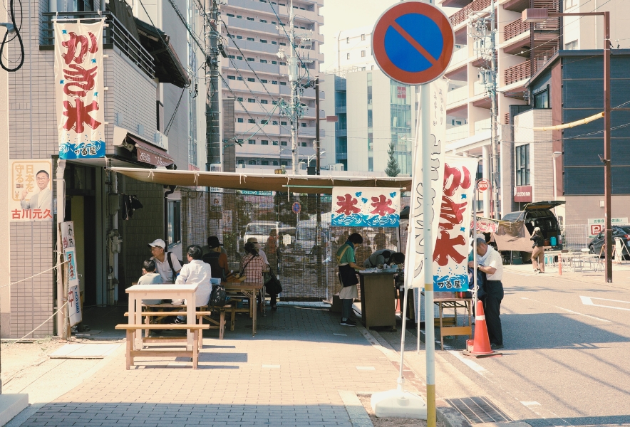覚王山日泰寺の縁日。参道の一角に並んだかき氷の旗と店先、木陰のベンチで涼をとる人々。