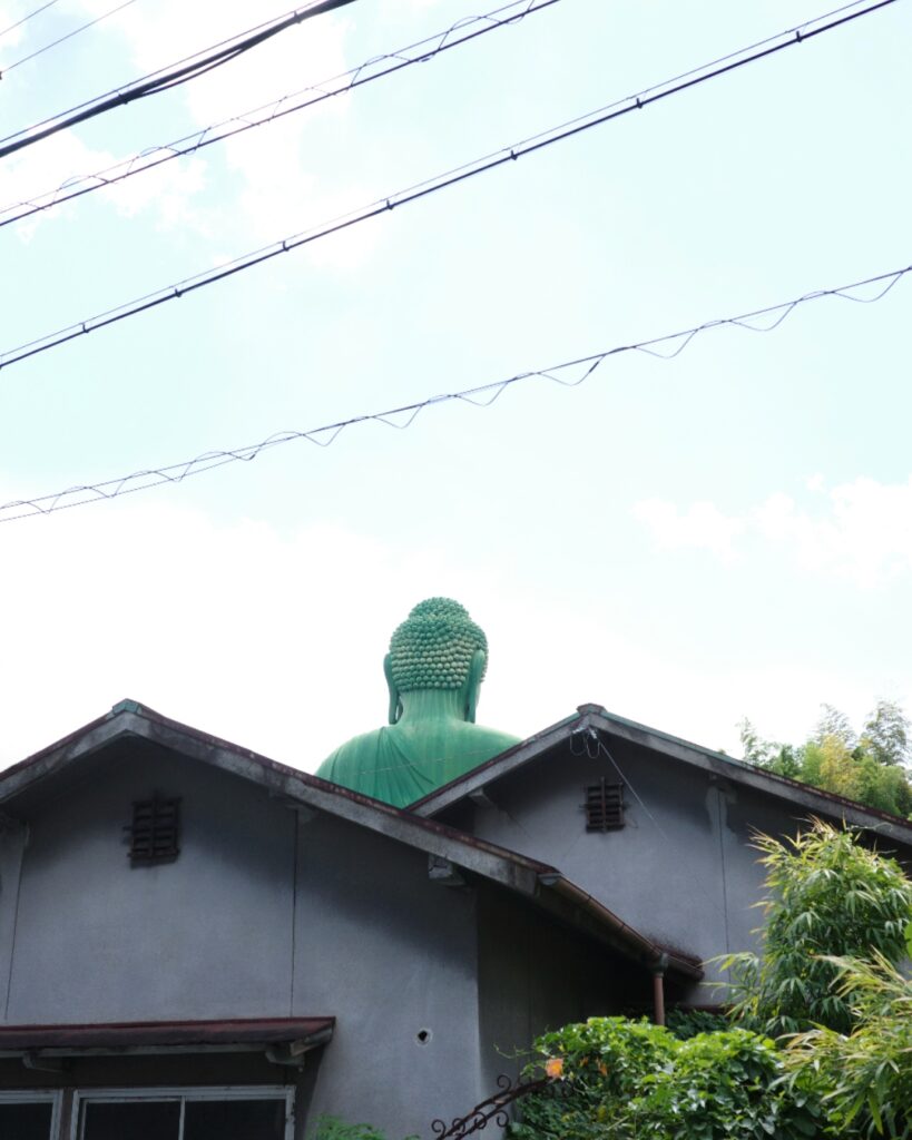 名古屋市千種区・桃厳寺の名古屋大仏が住宅の屋根越しに見える風景。緑色の巨大な後ろ姿が日常に溶け込む瞬間