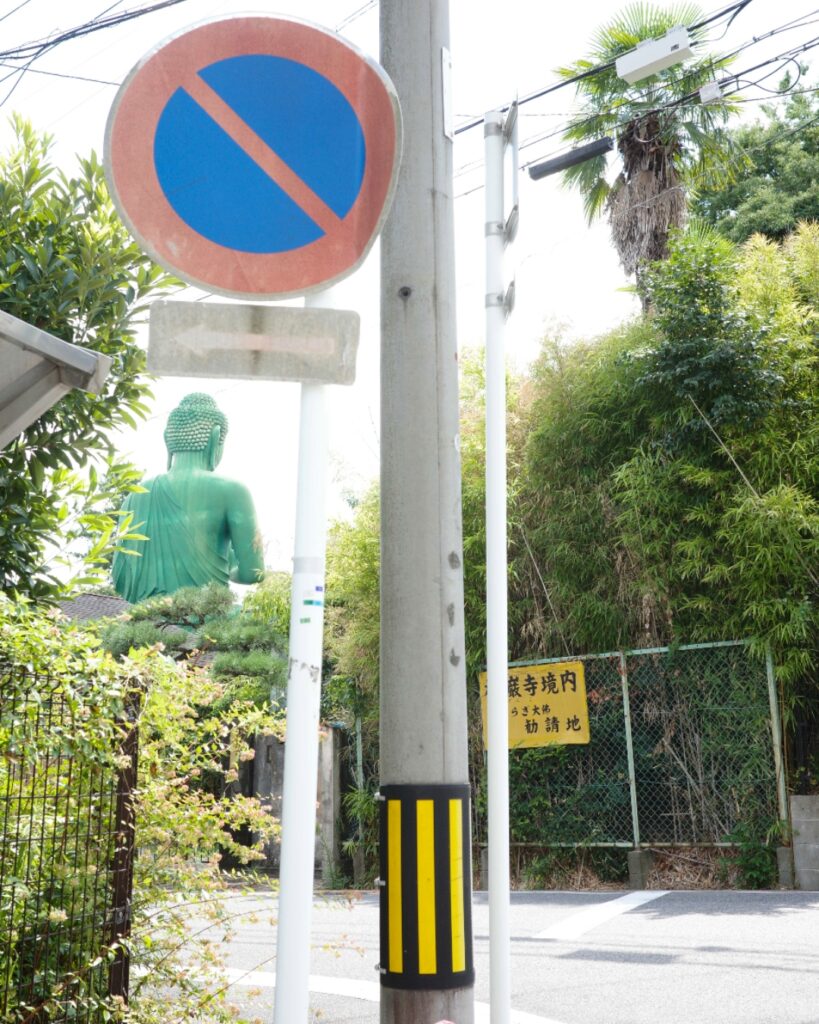 千種区・桃厳寺境内にある名古屋大仏の後ろ姿。住宅街の道路標識越しに見える、日常と非日常が交差する光景