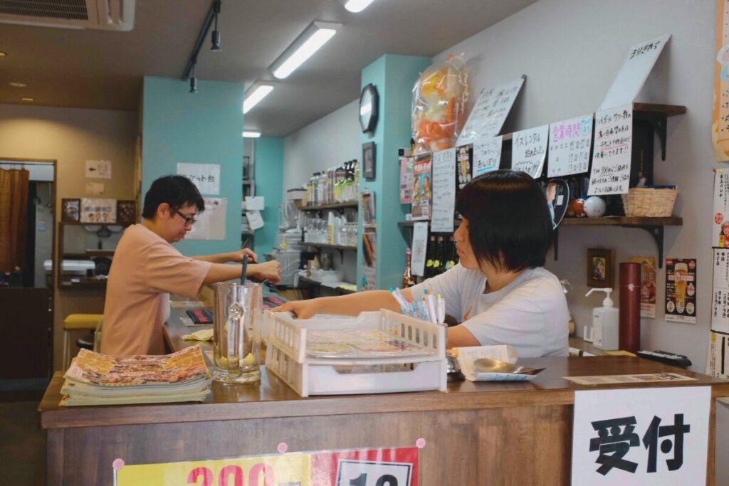 名古屋・今池の居酒屋せんべろ元気の受付カウンター。スタッフが注文対応を行い、日常の活気があふれる店内