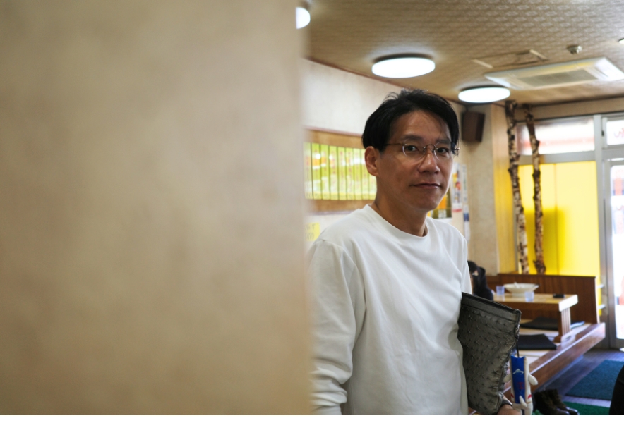 店内の柱越しに、台湾ラーメンを食べ終えて席を立つ客の様子。昔ながらの中華店の落ち着いた雰囲気が写る。