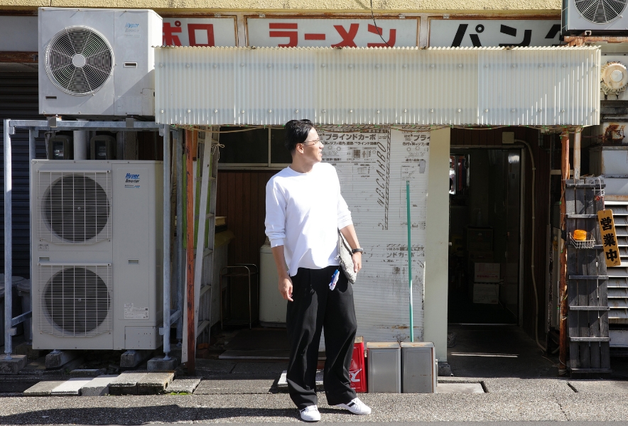 パンダラーメンの裏口の前に立つ客。年季の入った電源設備や看板とともに、通のみが知る裏口の存在が写し出されている。