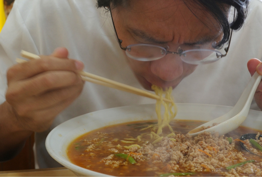 ジャンボ台湾ラーメンに顔を近づけ、勢いよく麺をすする瞬間。挽肉と湯気が丼を覆い、この店ならではの迫力が表れている。