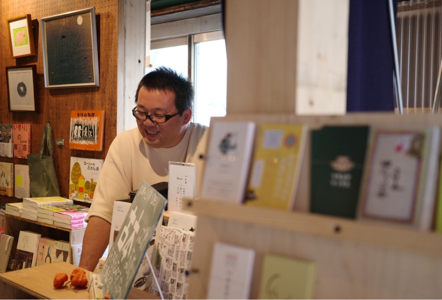 笠寺の本屋『ブタコヤブックス』で、カウンター越しに穏やかに本を紹介する船張真太郎さん。店内のあたたかな雰囲気が伝わる一枚。