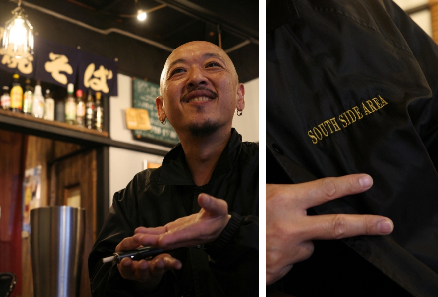 金山南の「KING焼きそば」で話す羽鳥浩二（King Papa）さん。胸元には“SOUTH SIDE AREA”と刺繍されたジャケット。金山の“南側”を象徴するように、朗らかな笑顔と手の動きが印象的。