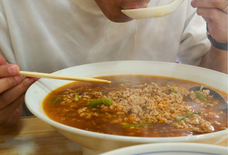 ジャンボサイズの台湾ラーメンのスープをすする瞬間。挽肉の層と湯気が際立ち、熱さと香りが伝わる。