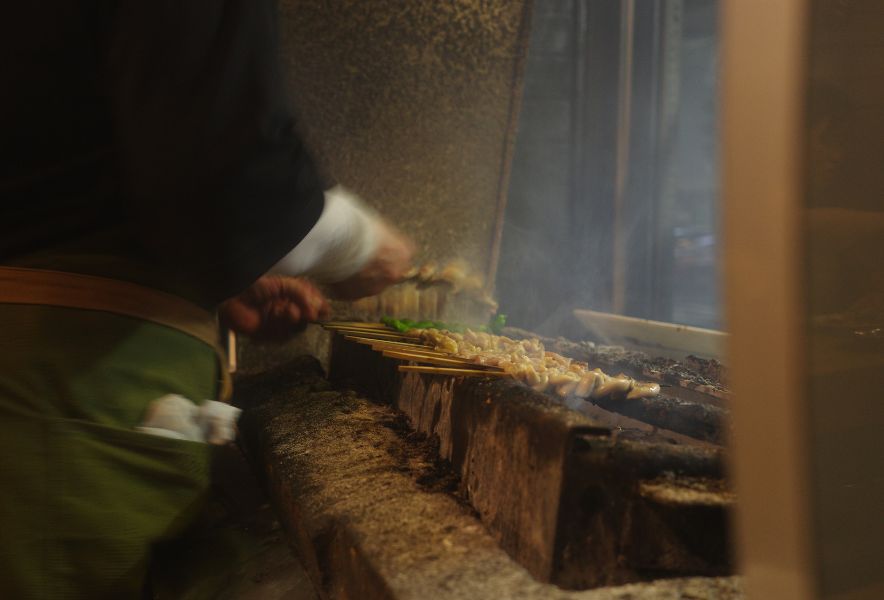 「なかの」の焼き場で串を焼く様子。煙の中で職人が串を返す昭和の酒場らしい光景。