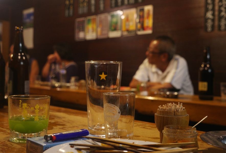 大曽根「なかの」のカウンターで、常連客が焼き鳥とビールを楽しむ様子。店の熱気と昭和の雰囲気を写した写真。