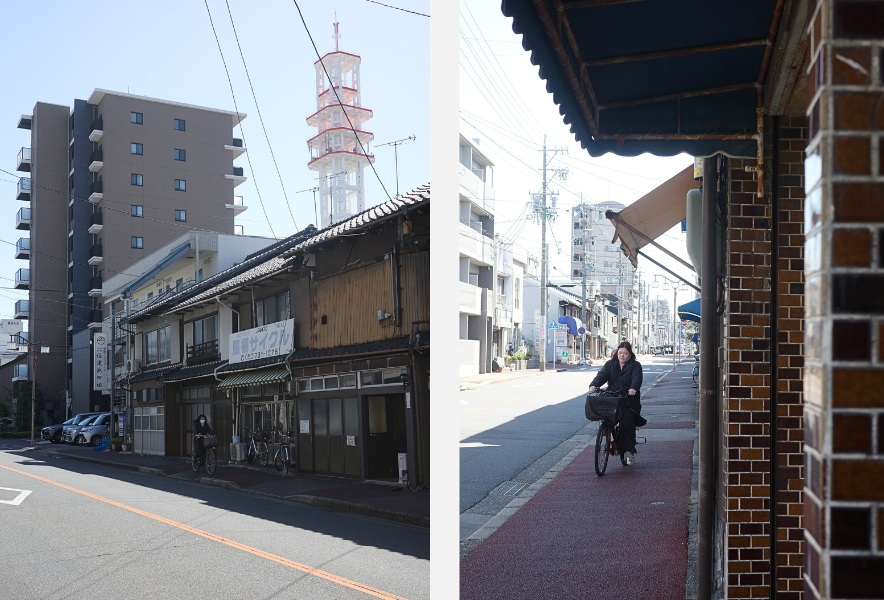 名古屋市昭和区・曙通り。住宅と商店が混ざる通りの奥に、街の塔が見える風景と軒先の影と光のあいだを、自転車が通り抜けていく。