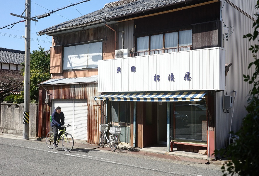 名古屋市昭和区・曙通りに面した素朴な外観の前を、自転車がゆっくり通り過ぎていく。