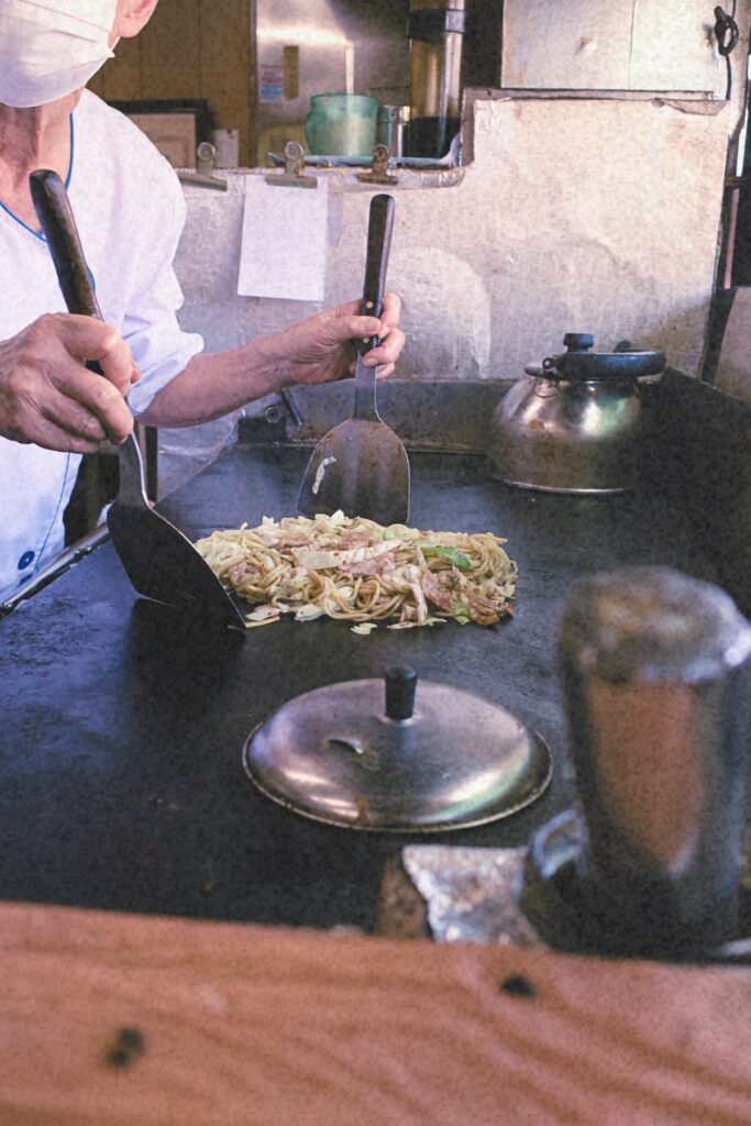 年季の入った鉄板の上で焼きそばを仕上げる板鼻氷店のお母さん。変わらない手つきが、この店の味を支えていた。