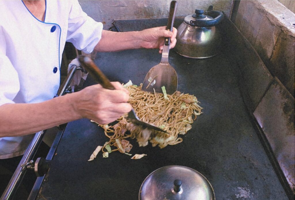 二本のヘラを使い、手際よく焼きそばを仕上げる板鼻氷店のお母さん。変わらない手つきが、この店の味を支えていた。