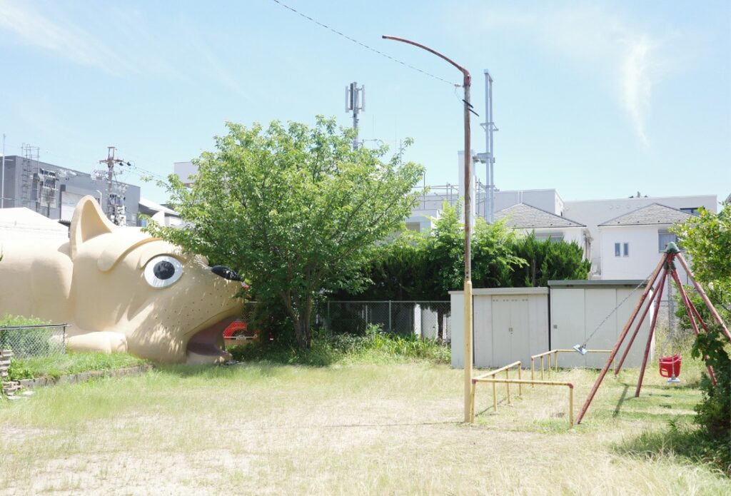 公園の遊具越しに見える犬型詰所。日常の風景に溶け込む少し不思議な存在。