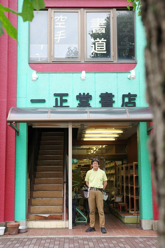 一正堂書店の入口に立つ店主、店舗外観