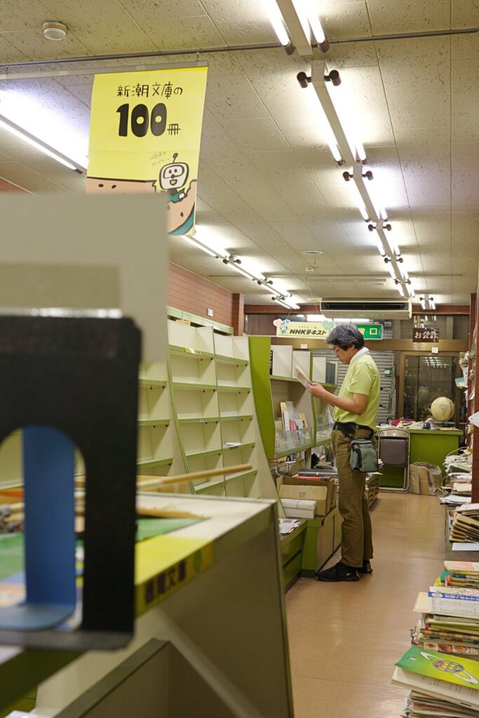 店内で本を手に取り確認する店主、空の棚が奥に続く