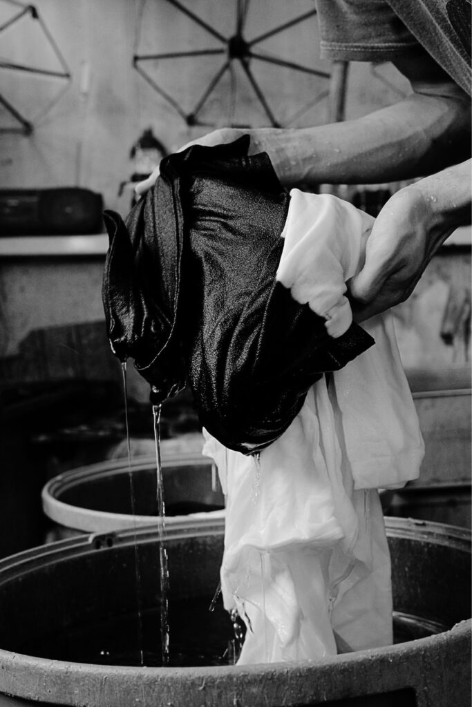 染め上がった白と黒の生地から水を切る黒紋付染の仕上げ工程