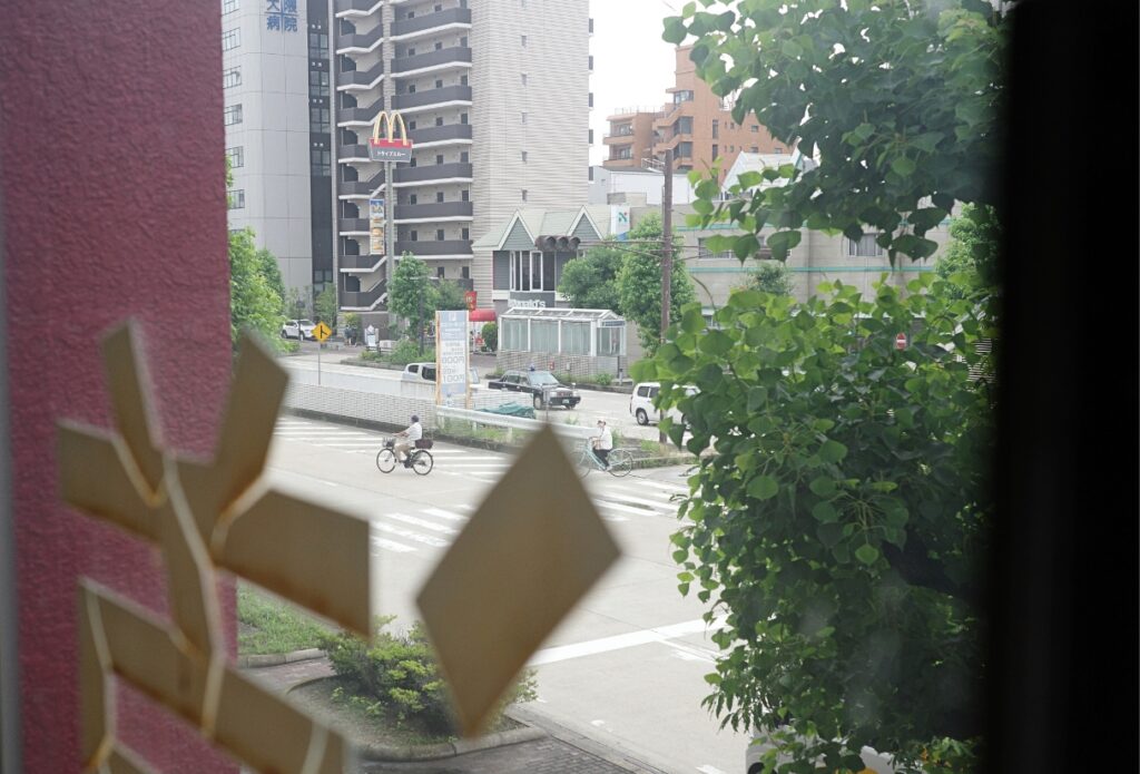 窓越しに見える大曽根の交差点と自転車で通る人々