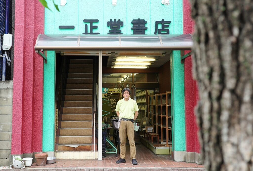 木の幹越しに見える一正堂書店の入口に立つ店主
