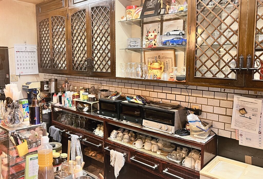 珈琲フランカのカウンターとキッチン。長年使われてきた木製収納やコーヒーカップが並ぶ純喫茶の風景。