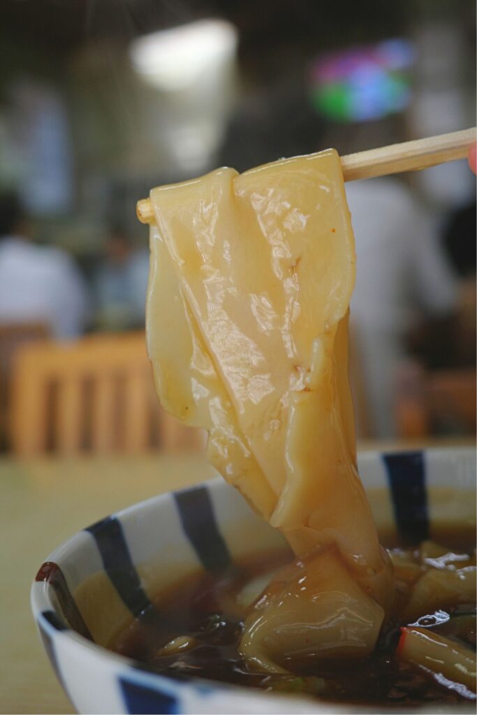 芳乃家名物の幅広い手打ちきしめんを箸で持ち上げた様子