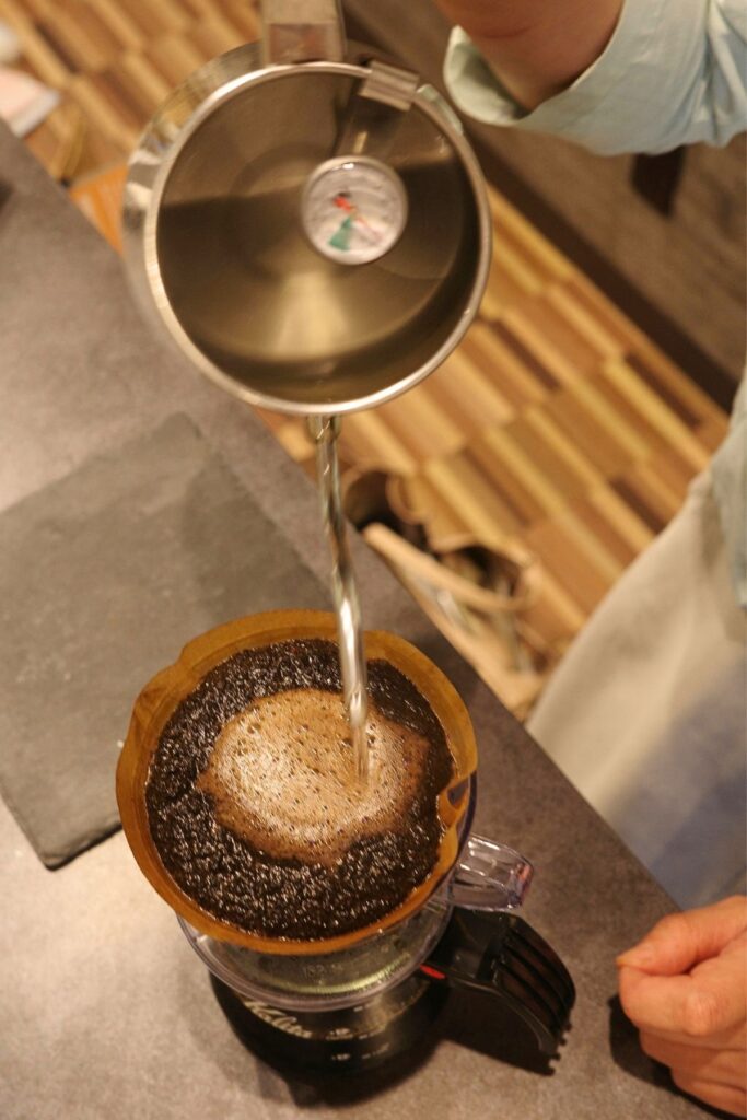 「Grains de café」のハンドドリップ。ドリップポットからコーヒー豆へゆっくりとお湯を注いで抽出する様子。