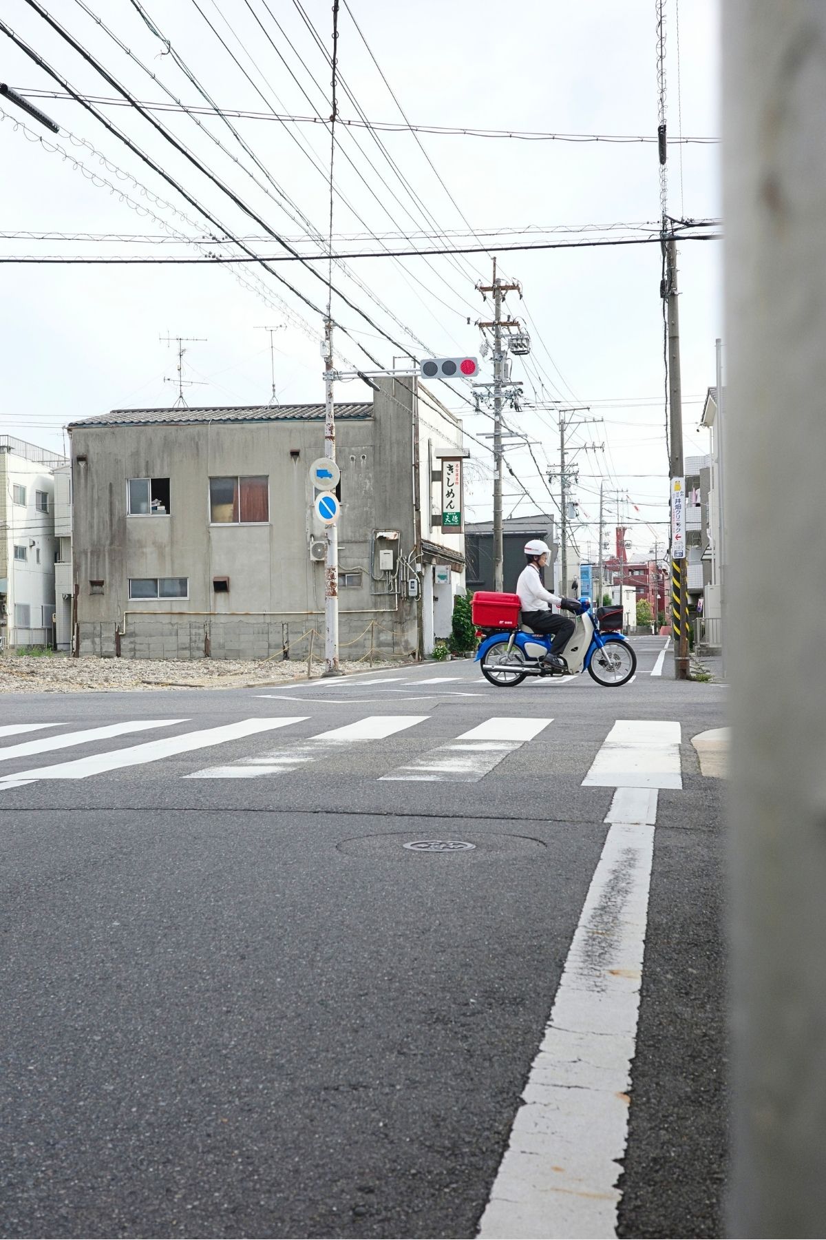 平屋が取り壊されたあとの交差点を横切るバイクと、ぽつんと残る古い建物