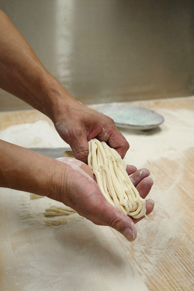 打ち粉をまとった手打ちうどんの麺を手に取る職人の手元