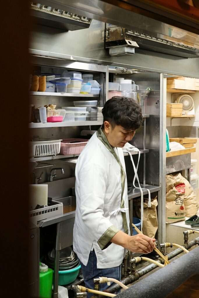 山本屋大久手店の厨房で、菜箸を手に味噌煮込みうどんをつくる5代目・青木晃佑さん
