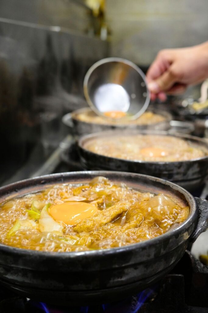 卵と油揚げがのった、ぐつぐつと煮立つ土鍋の味噌煮込みうどん