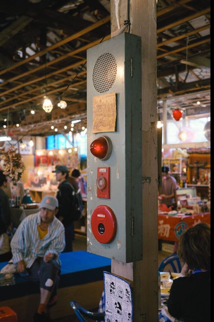 金城市場の柱に残る古い火災報知器と、朝市の店が並ぶ市場の中の様子