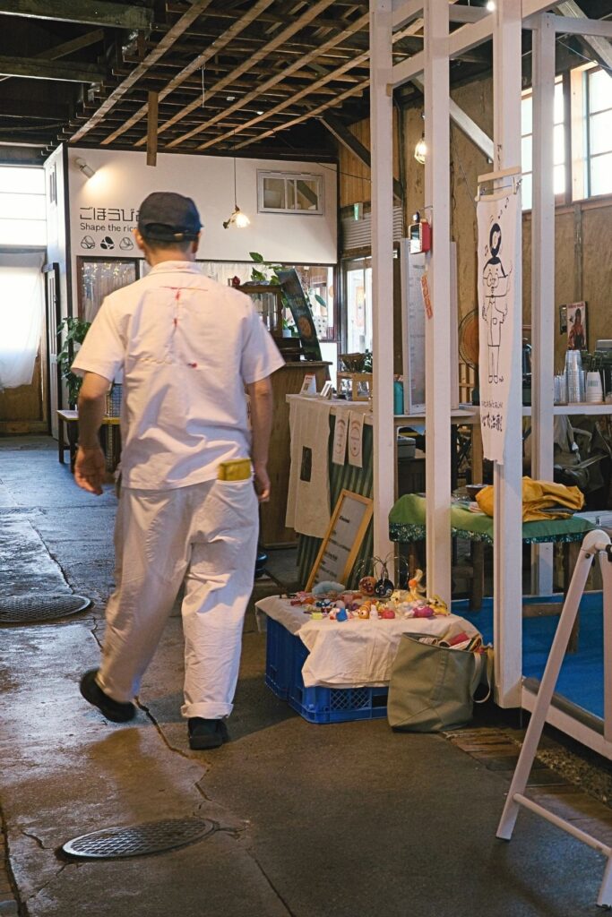 金城市場の中を歩く人と、いとだ治療院のオーナーと朝市の店が並ぶ通路