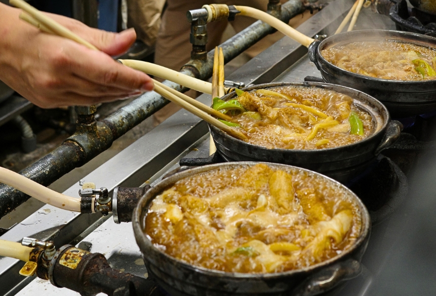 コンロに並んだ土鍋で煮込まれる山本屋大久手の味噌煮込みうどんと、菜箸を持つ手元