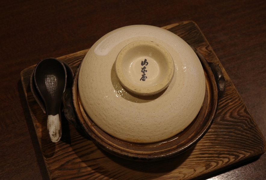 木の盆にのせた山本屋の土鍋。屋号入りのふたと黒いれんげ