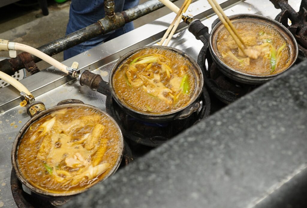 コンロに並び、ぐつぐつと煮立つ3つの土鍋の味噌煮込みうどん